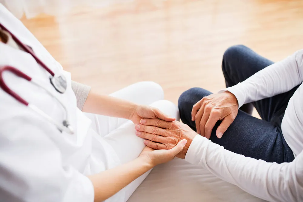 A physician holding a patient's hand during a home visit